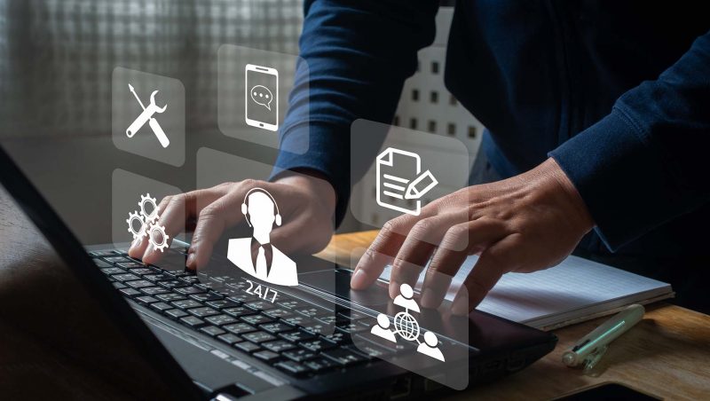 Person, die auf einem Laptop tippt, mit holografischen Symbolen, die technischen Support, Kommunikation, Dokumentenbearbeitung und globale Konnektivität darstellen